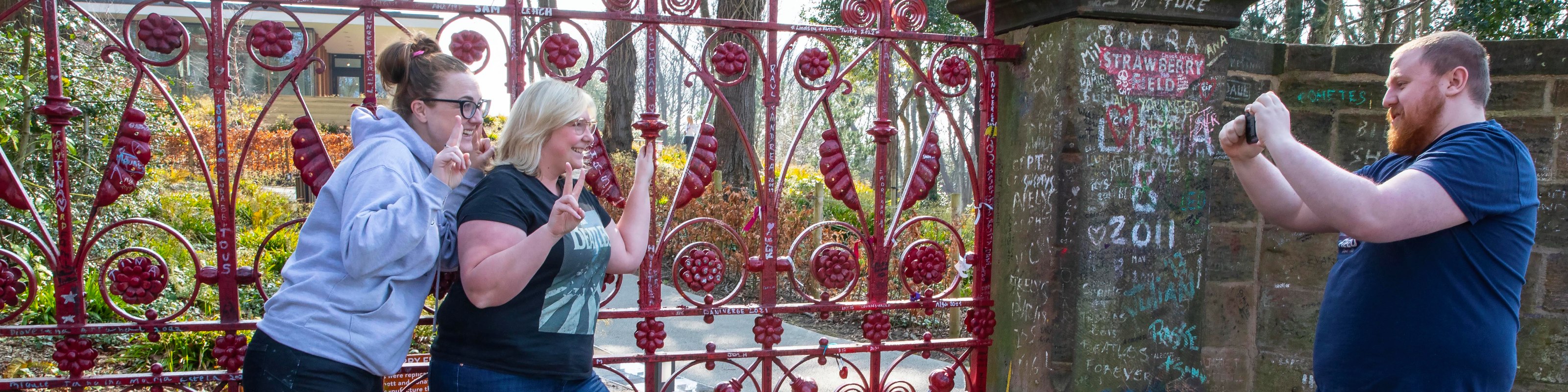 People standing outside the famous red gates at Strawberry Field taking a photo