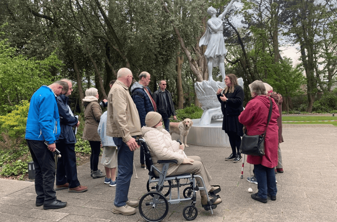 A group of people gather around the Ukrainian Peace Monument. One has a guide dog.